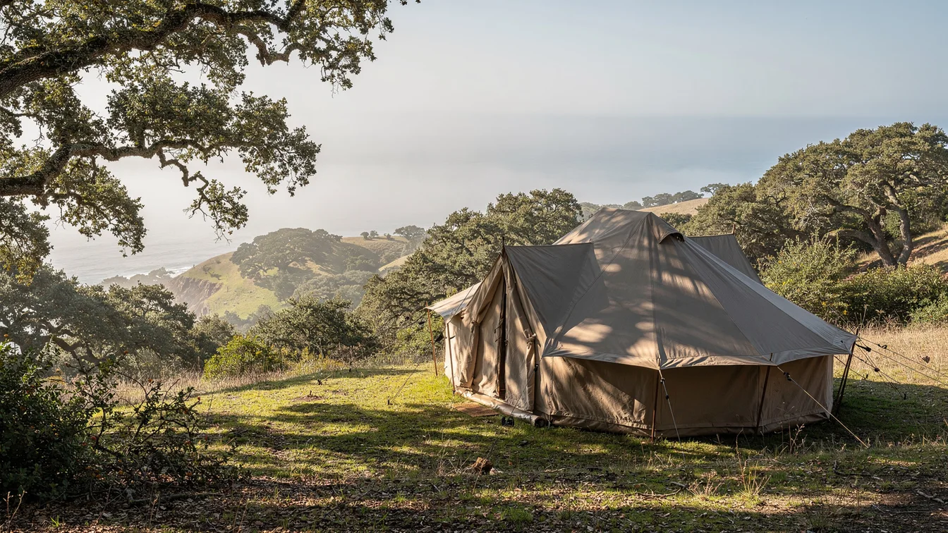 A canvas tent on a hillside with coastal oak woodland and distant ocean mist