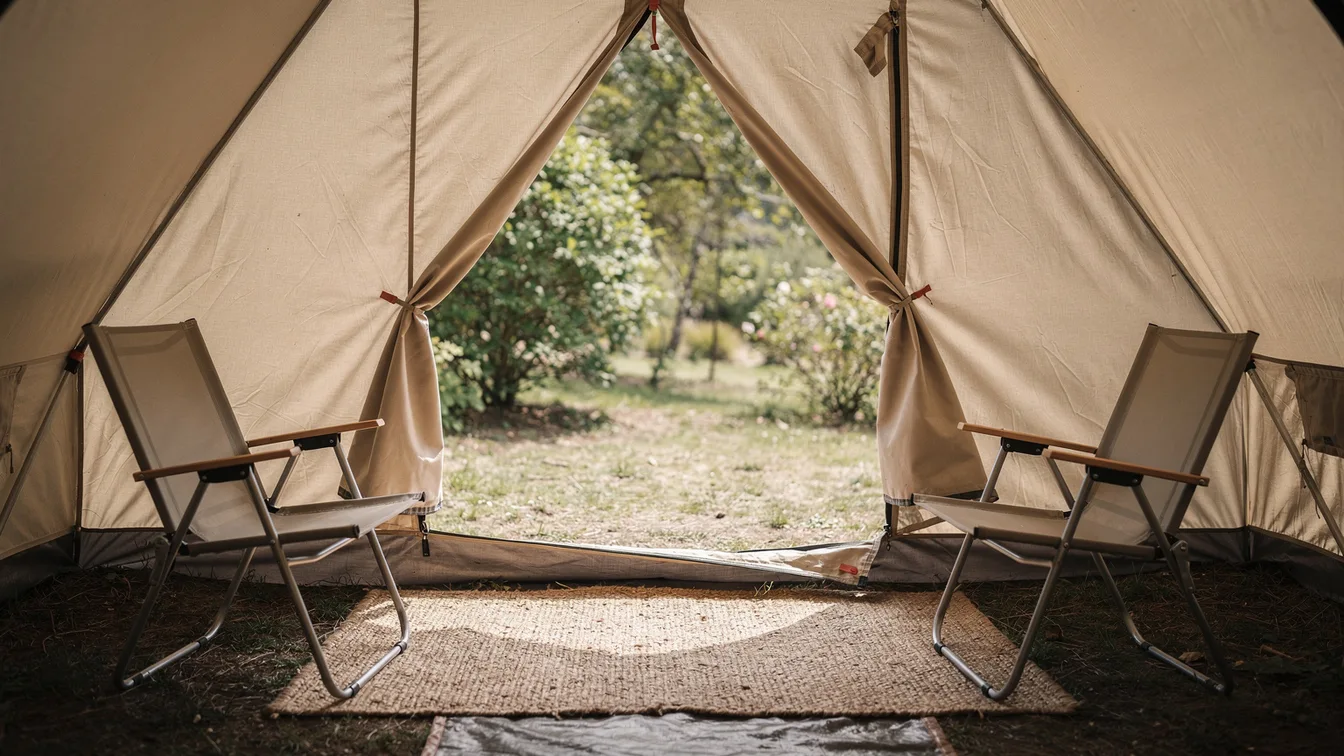 An inviting tent entrance with a woven mat and two camping chairs, leafy campsite beyond