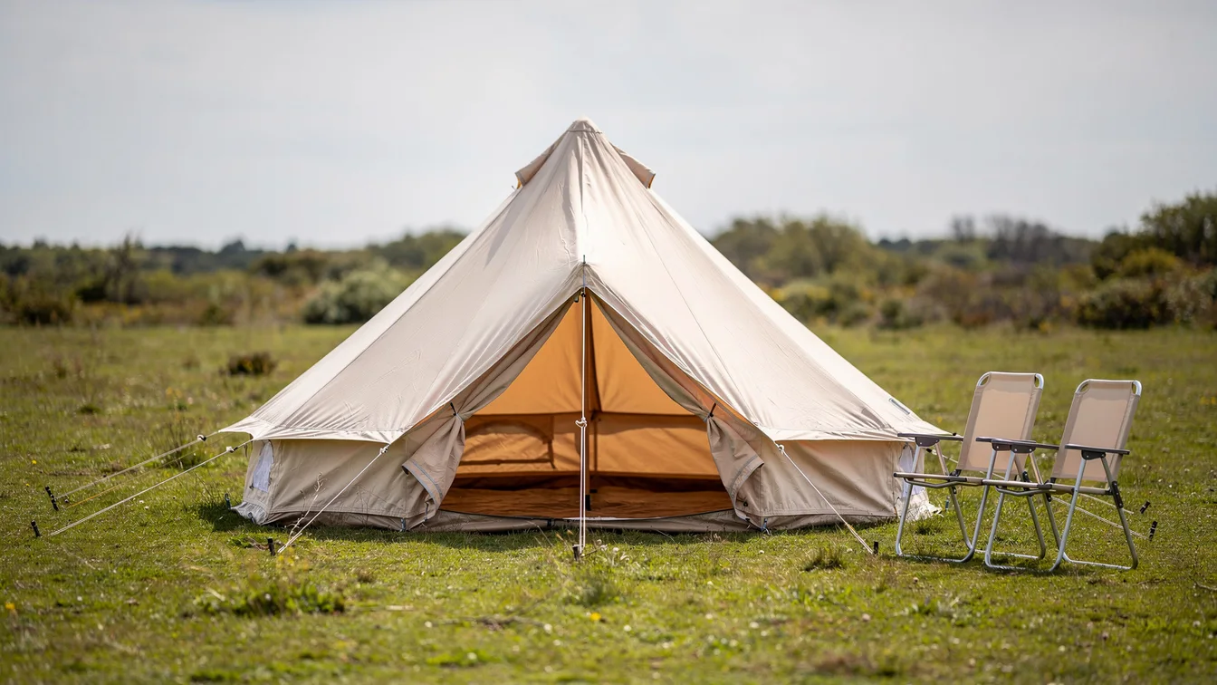 A canvas bell tent tensioned on grass with guy lines, camping chairs nearby